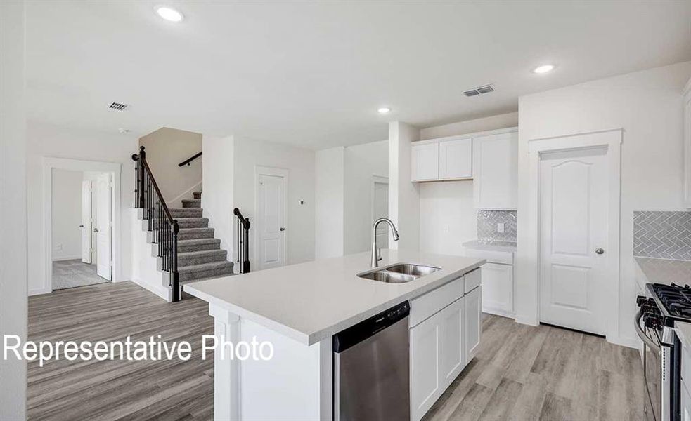 Kitchen with light wood-type flooring, sink, an island with sink, appliances with stainless steel finishes, and white cabinets