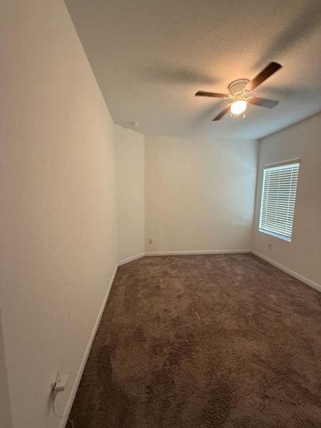 A well-lit bedroom features plush carpeting and an overhead ceiling fan for comfort.