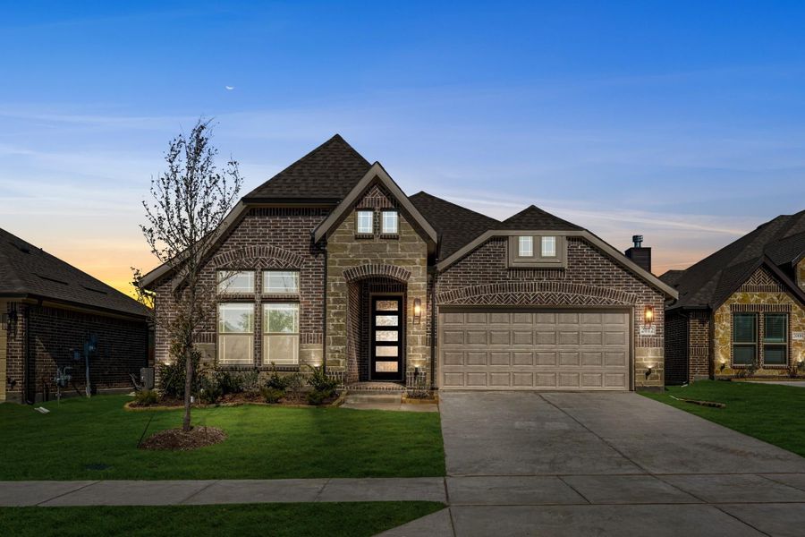 Single-story brick home with arched entry, two-car garage, and manicured lawn at dusk Single-story brick home with arched entry, two-car garage, and manicured lawn at dusk