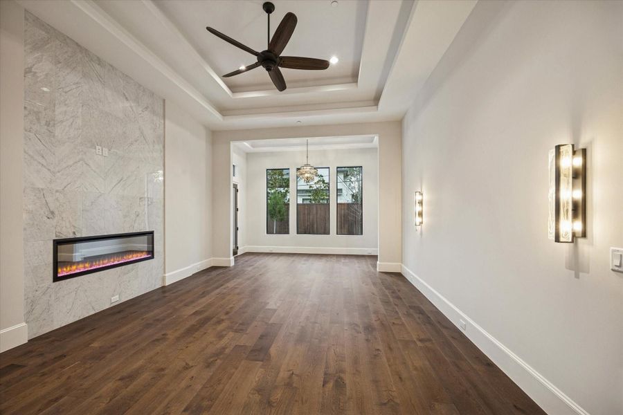 Expansive first floor primary suite featuring tray ceilings, a sleek linear firepace, hardwood floors, with serene backyard views and private access to the pool and outdoor living spaces. Expansive first floor primary suite featuring tray ceilings, a sleek linear firepace, hardwood floors, with serene backyard views and private access to the pool and outdoor living spaces.
