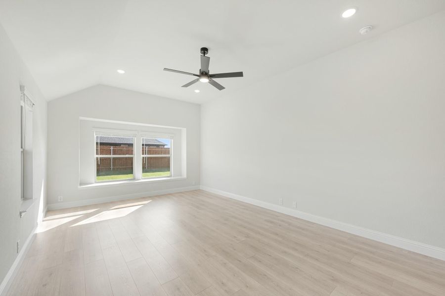 Empty room with vaulted ceiling, ceiling fan, light wood floors, and backyard-facing window