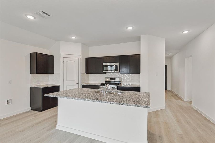 Kitchen with sink, an island with sink, backsplash, stainless steel appliances, and light hardwood / wood-style flooring