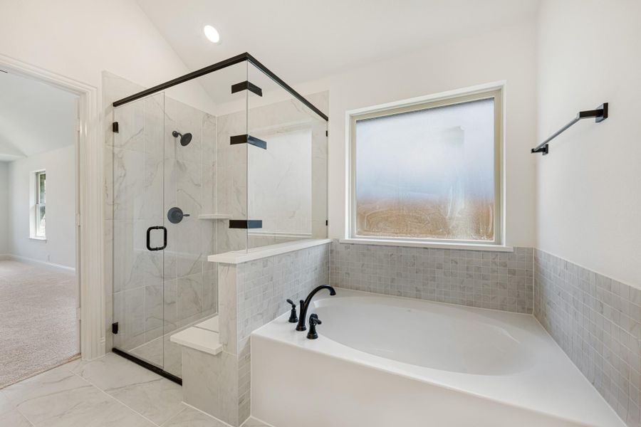 Master bathroom with soaking tub, glass-enclosed marble shower, and black fixtures on white tile floors