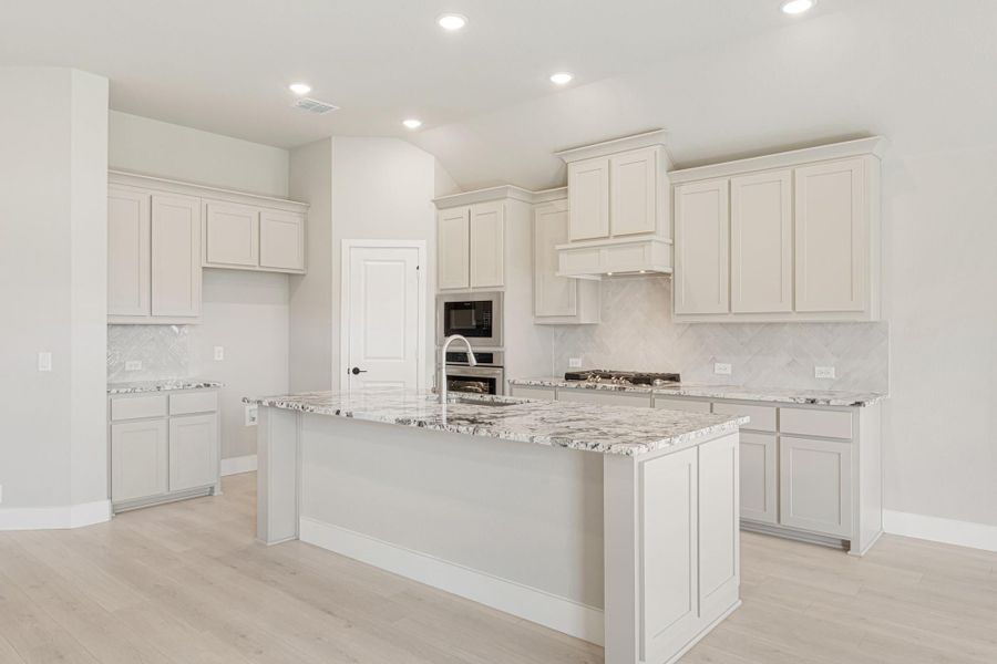 Kitchen with large center island, granite countertops, white cabinets, herringbone tile backsplash, and stainless steel appliances