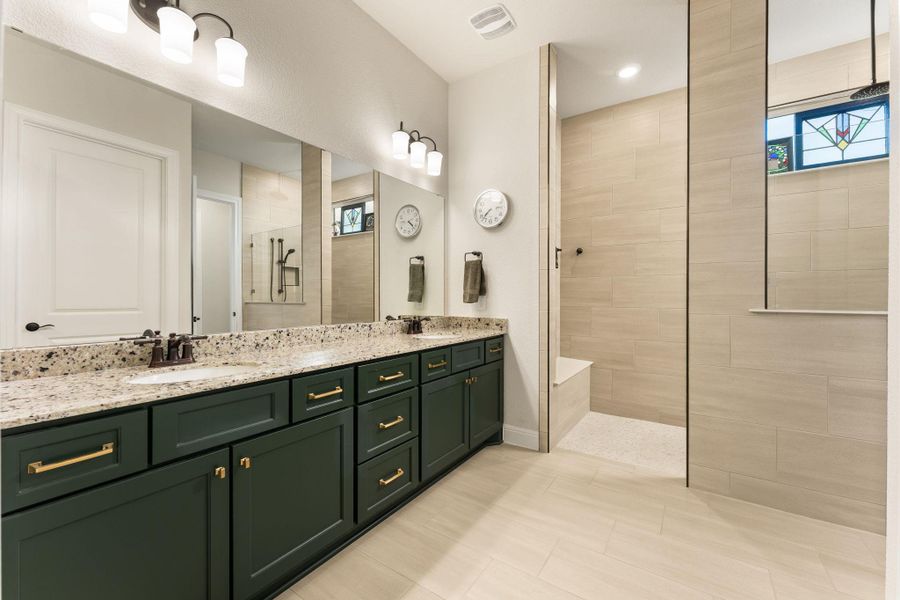 The stylish primary bath also features many upgrades, including a large shower with a bench, rain shower head and wand shower head. There are upgraded Crema Pearl granite counters, upgraded Ripe Olive cabinets, and upgraded Persuade Beige and Iconic Cape Gray tile. The upgraded 12x24 floor tile is Persuade Beige. The stylish primary bath also features many upgrades, including a large shower with a bench, rain shower head and wand shower head. There are upgraded Crema Pearl granite counters, upgraded Ripe Olive cabinets, and upgraded Persuade Beige and Iconic Cape Gray tile. The upgraded 12x24 floor tile is Persuade Beige.