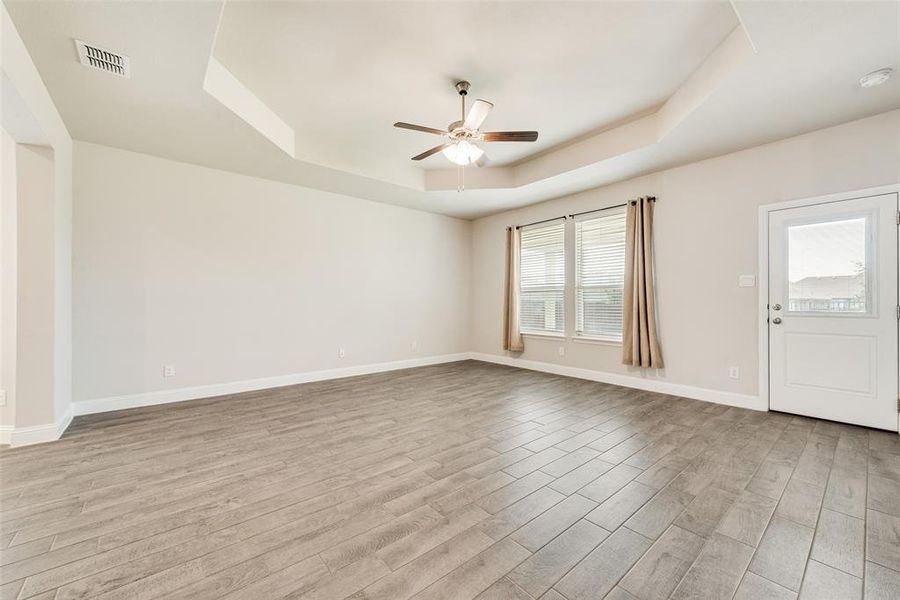 Spare room with a raised ceiling, light wood-type flooring, and a ceiling fan