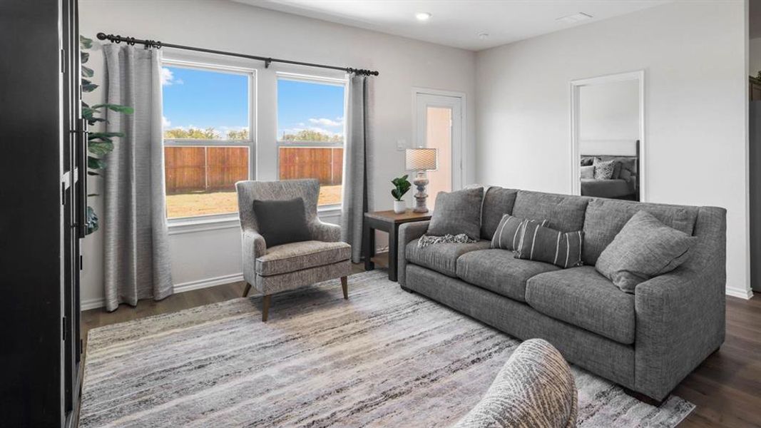 Spacious living area featuring wood-finish flooring, light-colored walls, and large windows overlooking a fenced yard