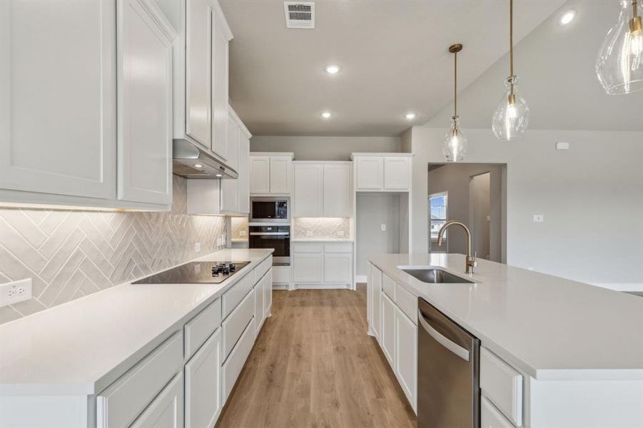 Kitchen with stainless steel appliances, sink, white cabinetry, and a kitchen island with sink