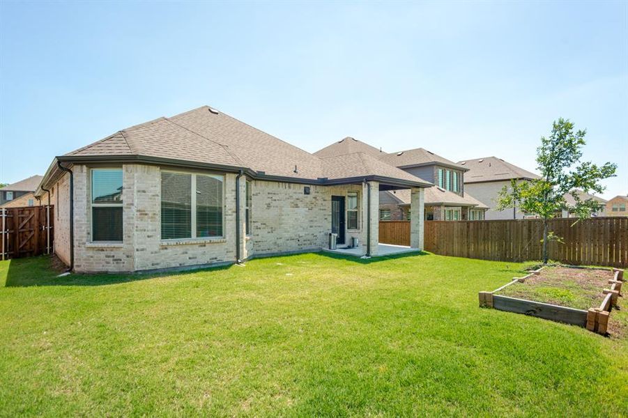 Spacious backyard featuring a covered patio, extensive lawn, wood privacy fencing, and a raised garden bed