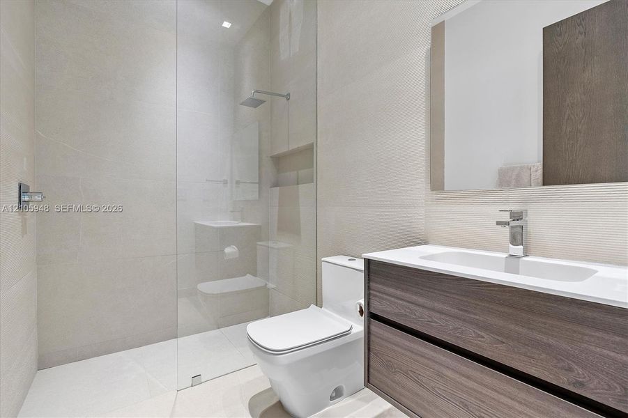 Floating vanity with wood-finish cabinetry, white countertop, integrated sink, rainfall shower head, and full-height glass shower panel