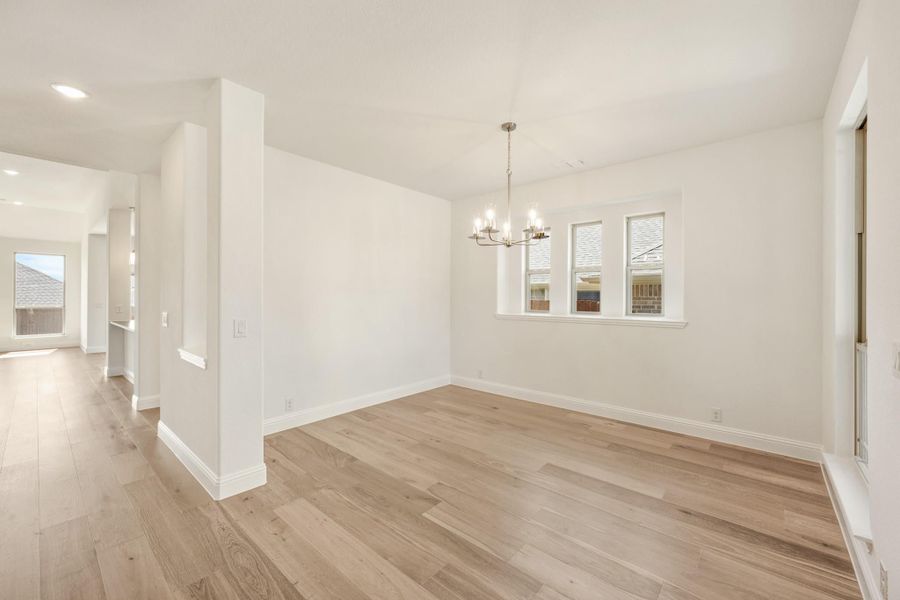 Empty dining room with light hardwood floors, chandelier, and triple window with white walls Empty dining room with light hardwood floors, chandelier, and triple window with white walls