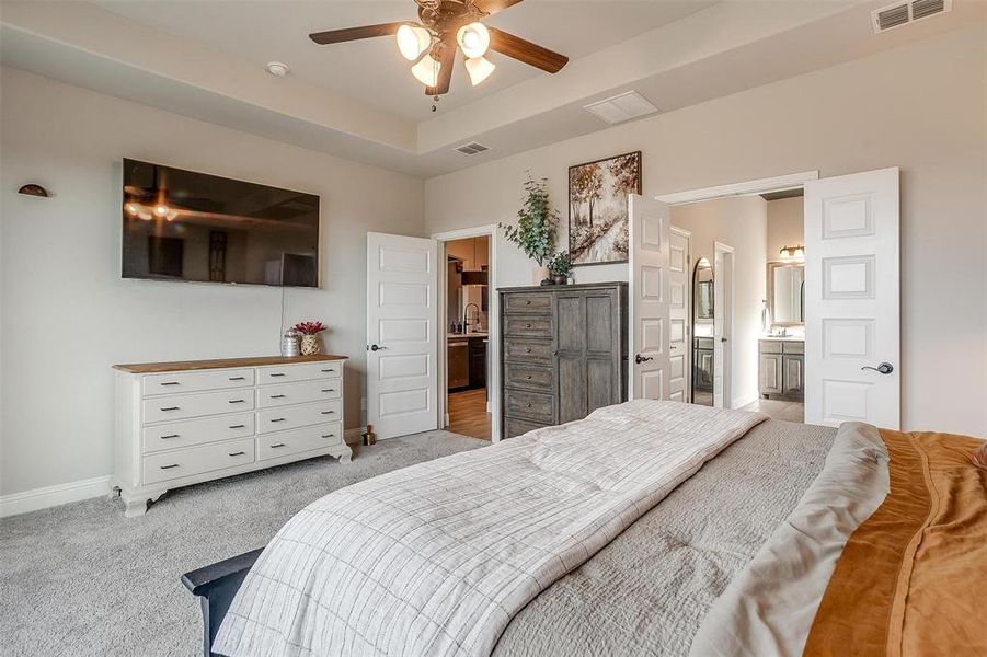 Bedroom with ensuite bathroom, ceiling fan, and light colored carpet