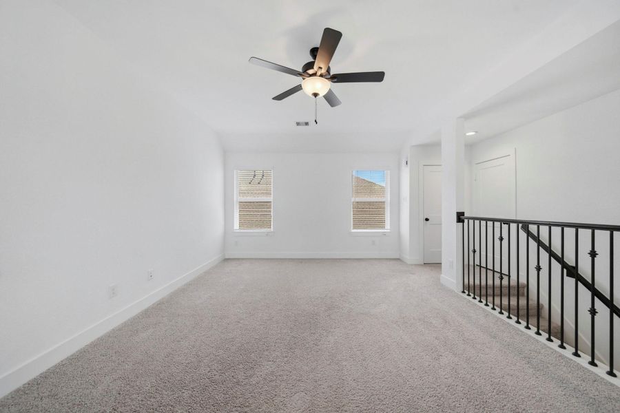 This spacious game room features plush carpet, a ceiling fan, and bright natural light!