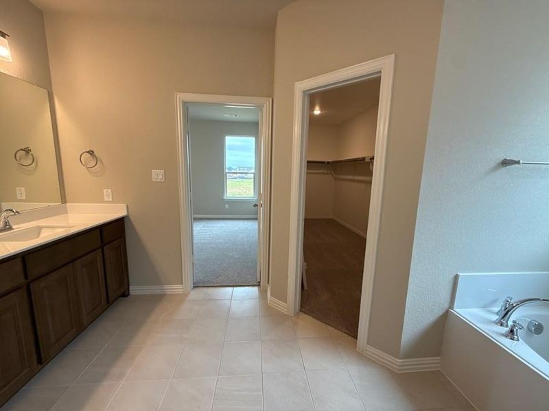 Bathroom featuring a dual vanity with dark wood cabinetry and light countertops, a built-in corner tub, and light-toned tile flooring