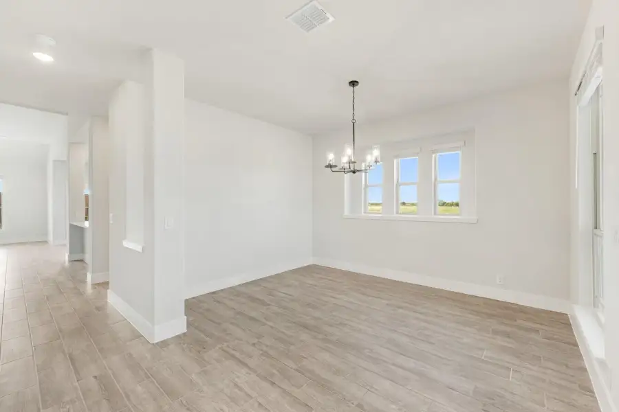 Empty dining room with light wood floors, chandelier, and double windows with natural light