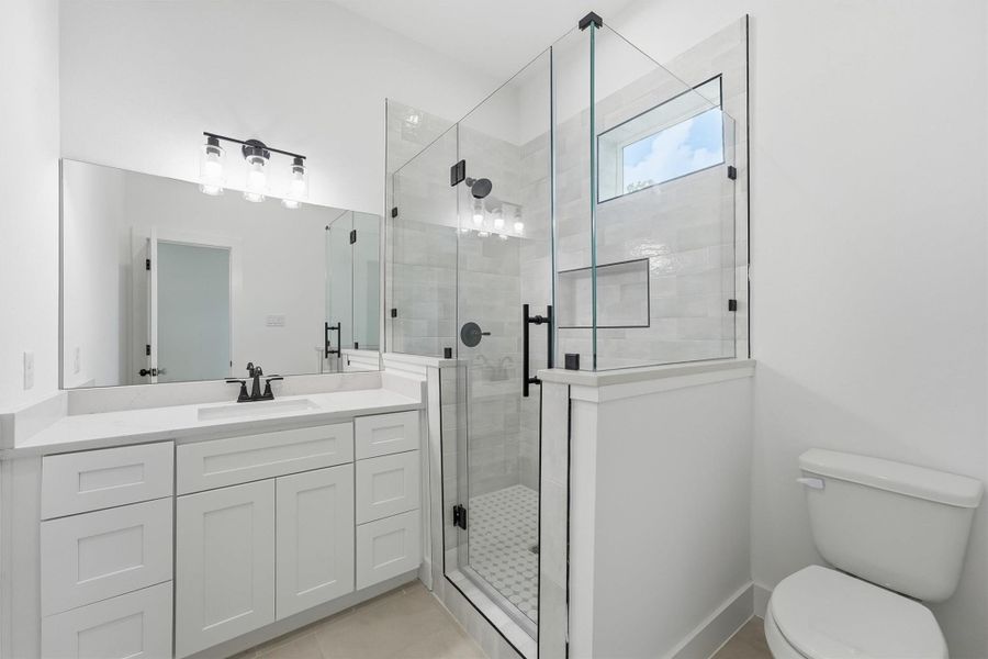 This beautifully finished full bath features quartz countertops, white shaker cabinetry, matte black fixtures, a frameless glass shower with subway tile surround, and a mosaic tile floor that adds the perfect finishing touch. This beautifully finished full bath features quartz countertops, white shaker cabinetry, matte black fixtures, a frameless glass shower with subway tile surround, and a mosaic tile floor that adds the perfect finishing touch.