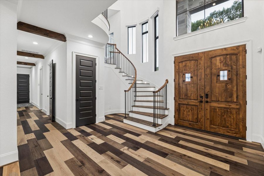 Stepping inside, you're greeted by a breathtaking foyer featuring soaring approximately 25-foot ceilings, abundant natural light, and a dramatic staircase that immediately captures your attention. Elegant chandeliers, rich hardwood flooring, and carefully curated architectural details create a spectacular first impression. This remarkable entry serves as the perfect introduction to a home where timeless design, luxury finishes, and exceptional craftsmanship are showcased at every turn.
