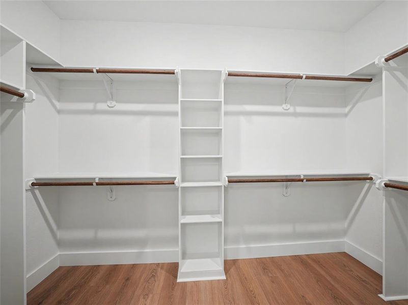 Walk-in closet featuring built-in shelving, multiple hanging rods, and wood-finish flooring Walk-in closet featuring built-in shelving, multiple hanging rods, and wood-finish flooring