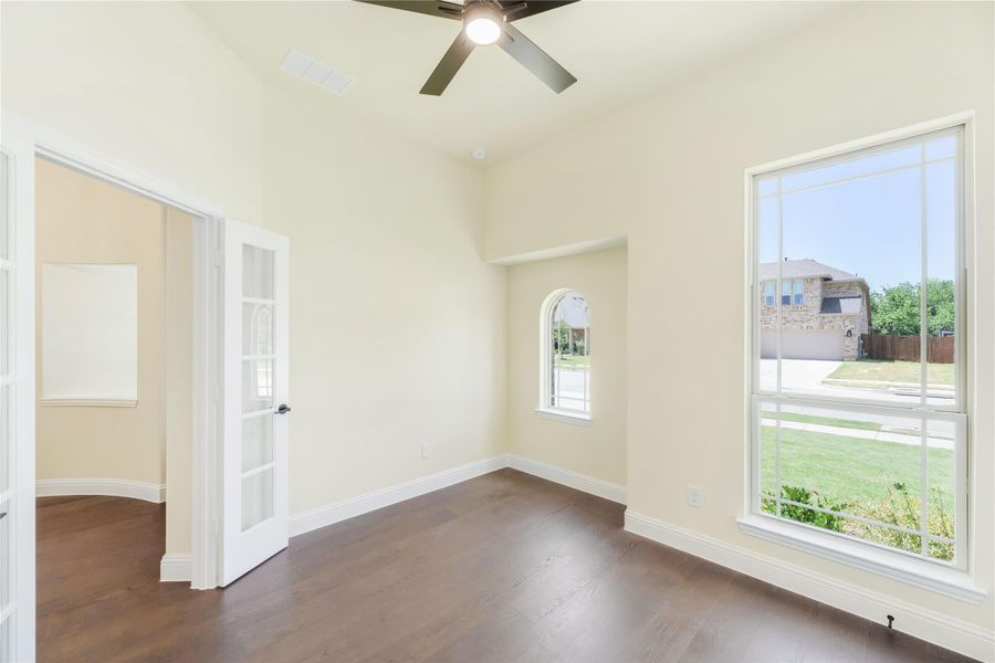 Empty room with dark hardwood floors, ceiling fan, large windows, and a French door Empty room with dark hardwood floors, ceiling fan, large windows, and a French door