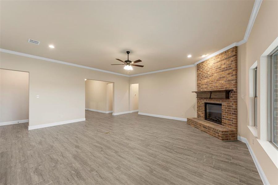 Unfurnished living room with ceiling fan, light wood-style flooring, a fireplace, baseboards, and crown molding