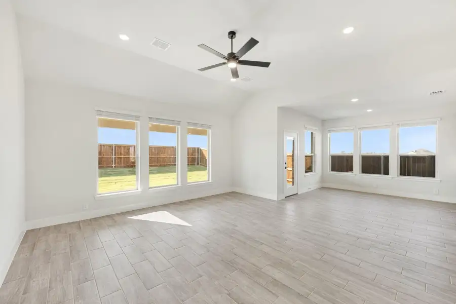 Open living area with vaulted ceiling, ceiling fan, wood-look tile floors, and large windows overlooking backyard