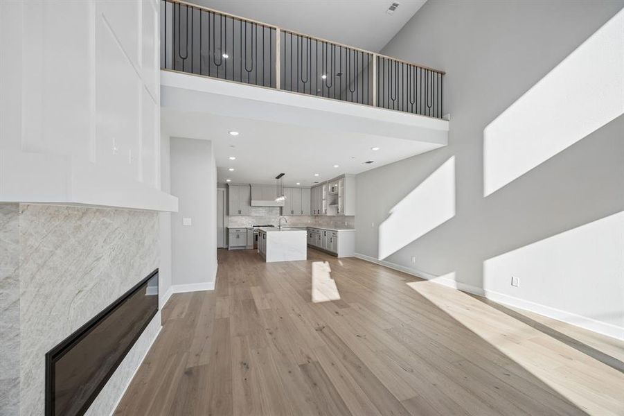 Unfurnished living room with light wood-type flooring, a glass covered fireplace, and a high ceiling Unfurnished living room with light wood-type flooring, a glass covered fireplace, and a high ceiling