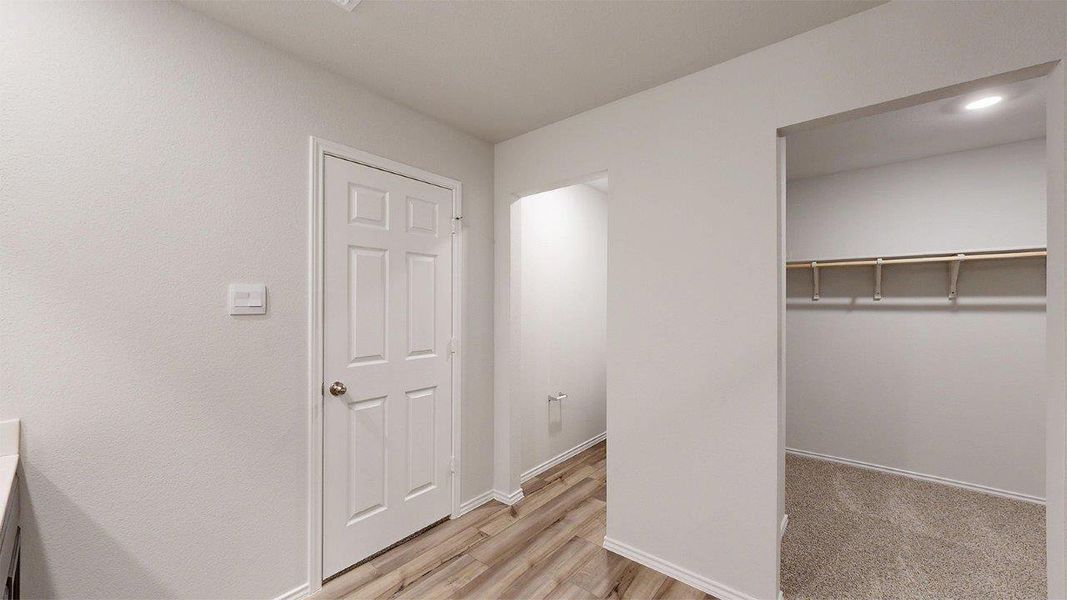 Interior hallway featuring wood-finish flooring, a white paneled door, and neutral wall finishes Interior hallway featuring wood-finish flooring, a white paneled door, and neutral wall finishes