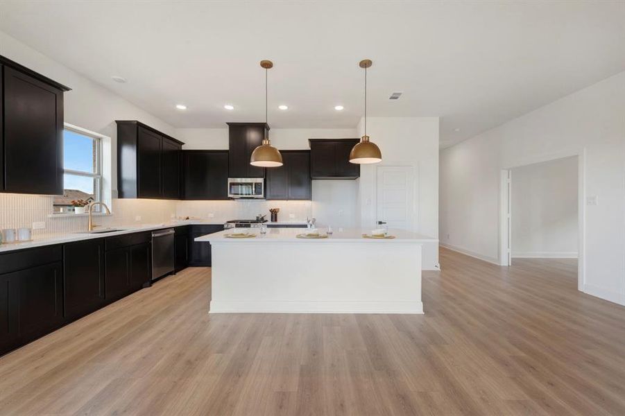 Kitchen with dark cabinetry, hanging light fixtures, a center island, stainless steel appliances, and decorative backsplash Kitchen with dark cabinetry, hanging light fixtures, a center island, stainless steel appliances, and decorative backsplash