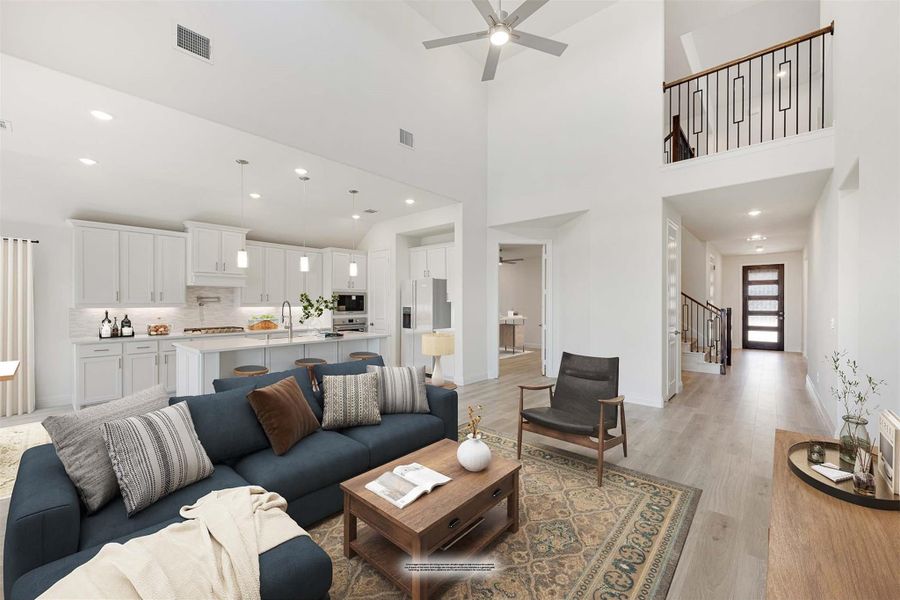 Open-concept living room with vaulted ceiling, ceiling fan, blue sofa, and kitchen visible in background with white cabinets Open-concept living room with vaulted ceiling, ceiling fan, blue sofa, and kitchen visible in background with white cabinets