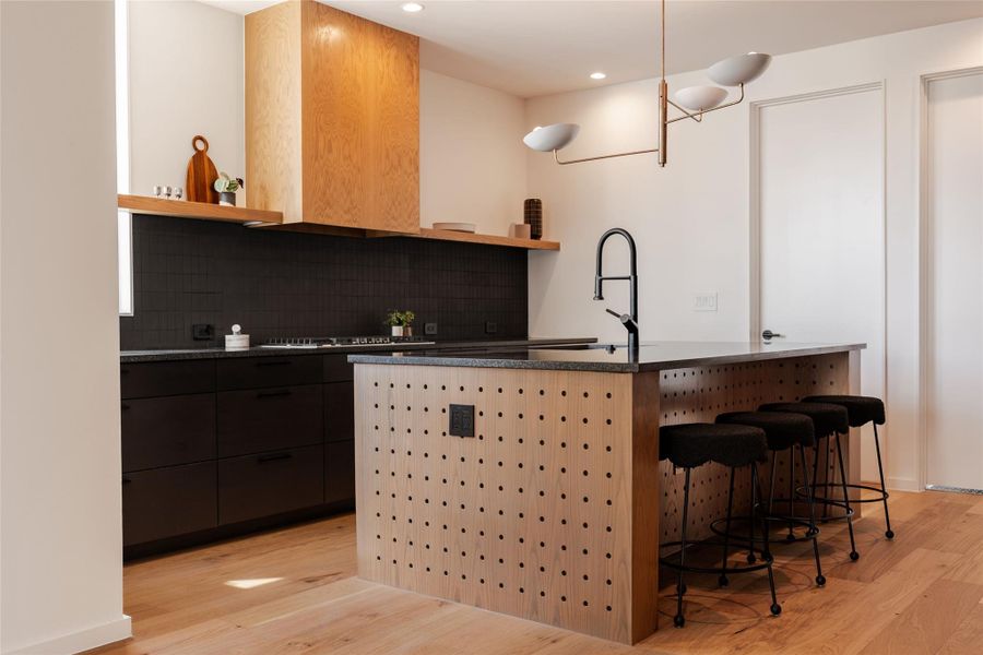 Kitchen featuring open shelves, backsplash, light wood-type flooring, a kitchen bar, and recessed lighting