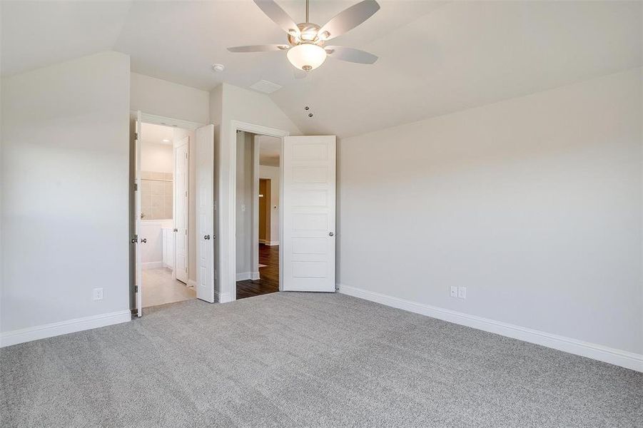 Unfurnished bedroom with carpet, vaulted ceiling, ceiling fan, and ensuite bathroom