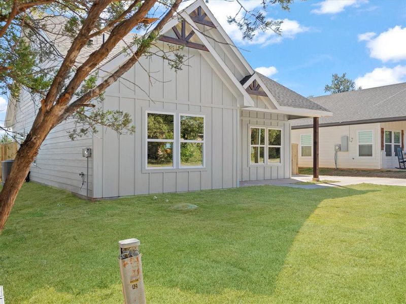 Rear view of property featuring board and batten siding, a yard, a patio, and roof with shingles Rear view of property featuring board and batten siding, a yard, a patio, and roof with shingles