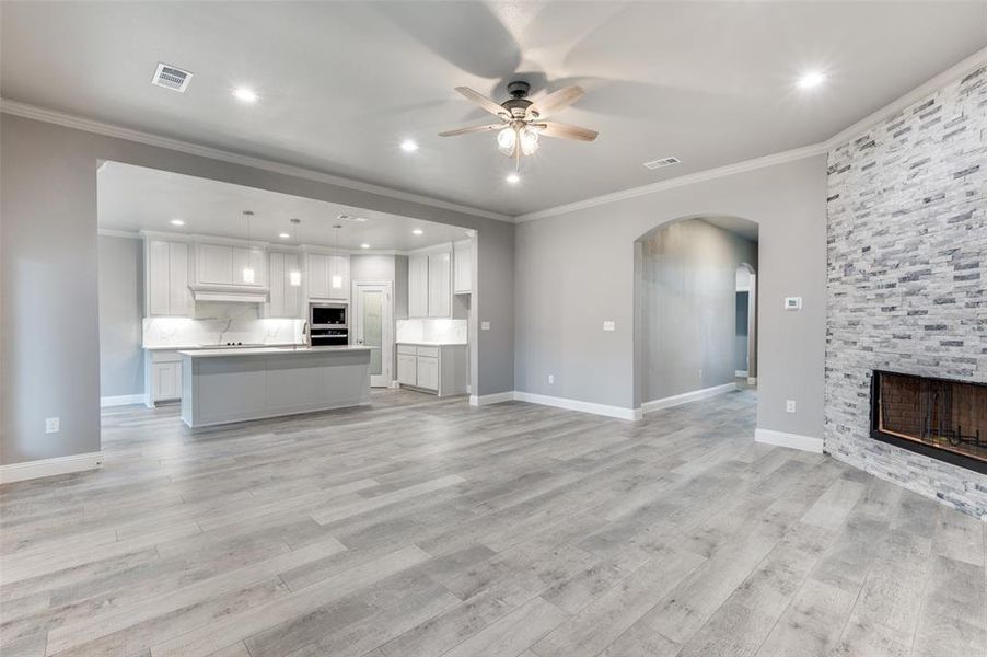 Unfurnished living room with crown molding, a fireplace, ceiling fan, and light hardwood / wood-style floors