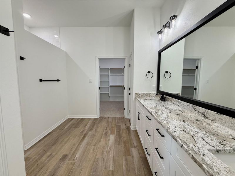 Bathroom featuring an extensive vanity with a light-toned countertop, dual sinks, and a large framed mirror