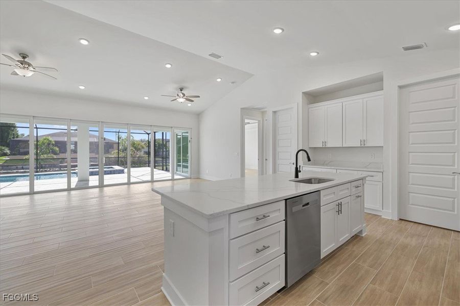 Kitchen with white cabinets, wood tiled floors, open floor plan, light stone countertops, and a center island with sink