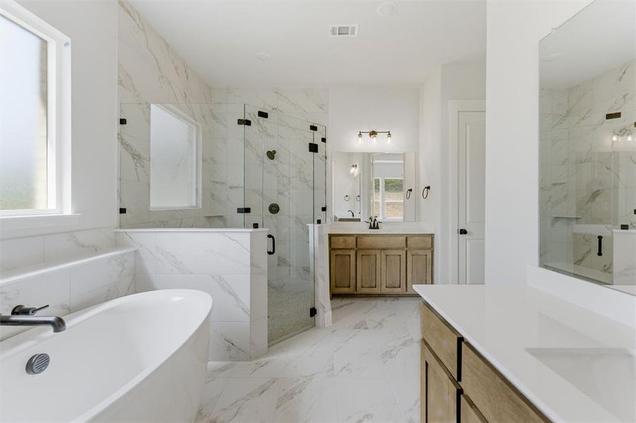 Full bathroom with two vanities, a marble finish shower, a freestanding tub, and light marble finish floors