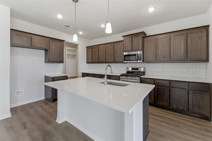 Modern kitchen featuring a large central island with a sink, quartz countertops, dark wood-finish cabinetry, stainless steel appliances, and wood-finish flooring