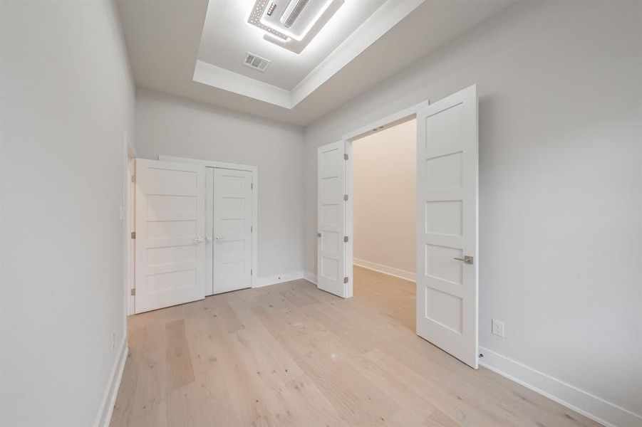 Unfurnished bedroom featuring light wood-type flooring, a tray ceiling, and a closet
