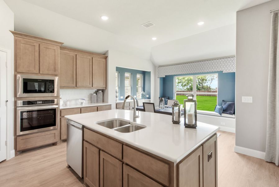 Kitchen with center island, double sink, light wood cabinets, and stainless steel appliances opening to a breakfast nook
