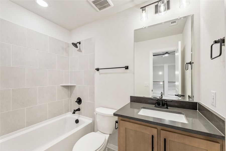 Bathroom with tiled tub-shower combo, wood vanity with dark countertop, and black fixtures Bathroom with tiled tub-shower combo, wood vanity with dark countertop, and black fixtures