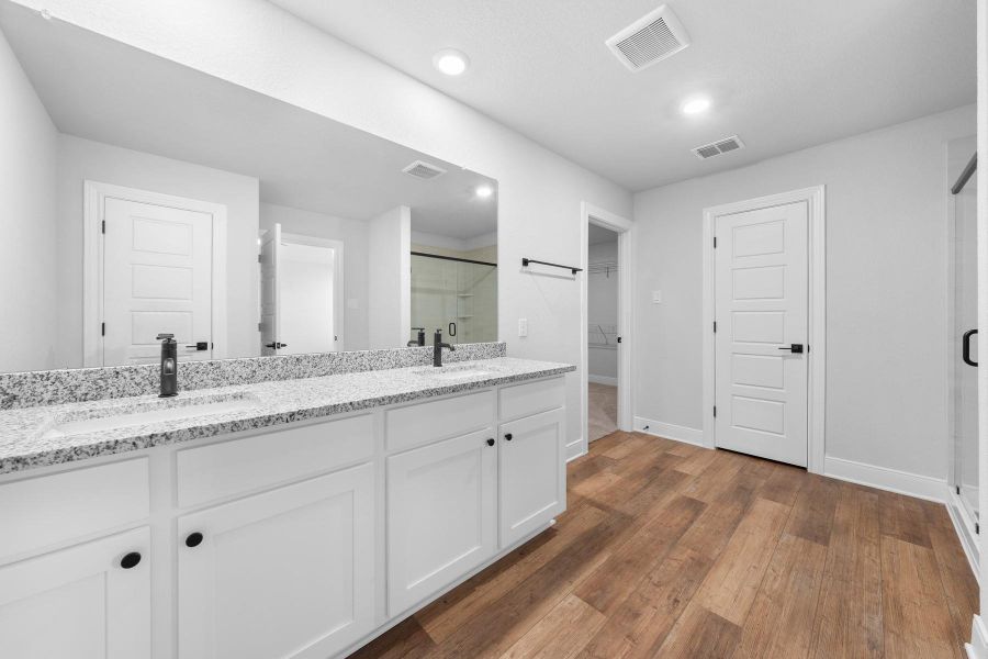 Full bathroom with double vanity, a shower stall, and dark wood finished floors