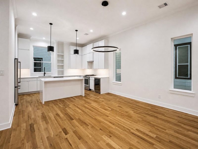 The contemporary kitchen is beautifully appointed with tall white cabinetry, stainless steel appliances, sleek countertops, and a generous center island. Black pendant lights provide dramatic contrast, while a modern faucet, under-cabinet lighting, and abundant storage enhance functionality. Warm wood flooring softens the crisp palette and connects the kitchen seamlessly with the surrounding living spaces. The contemporary kitchen is beautifully appointed with tall white cabinetry, stainless steel appliances, sleek countertops, and a generous center island. Black pendant lights provide dramatic contrast, while a modern faucet, under-cabinet lighting, and abundant storage enhance functionality. Warm wood flooring softens the crisp palette and connects the kitchen seamlessly with the surrounding living spaces.