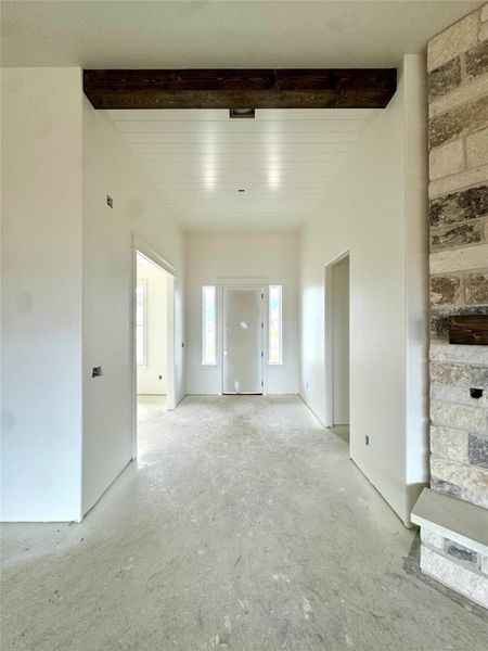 A spacious entry hallway features a fireplace and natural light, highlighting the high ceilings and unique beam details.