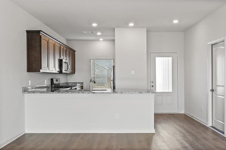 Kitchen featuring dark brown cabinets, wood finished floors, stone countertops, stainless steel appliances, and a sink