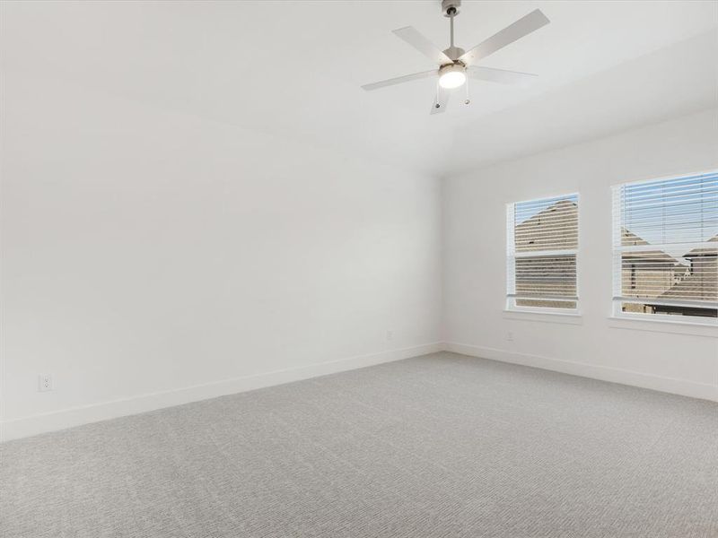Primary bedroom with light colored carpet and ceiling fan