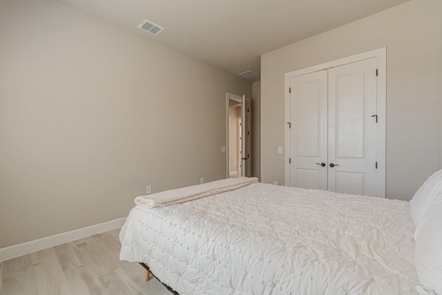 Bedroom with light wood finished floors, visible vents, baseboards, and a closet