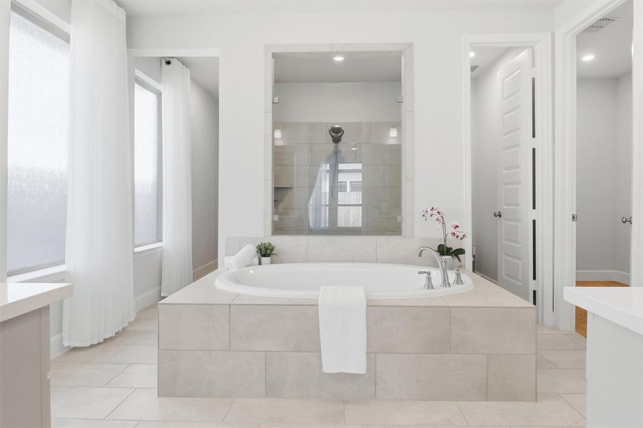 Designed with relaxation in mind, the spa-inspired primary bath centers around a luxurious soaking tub framed by elegant tilework. The open layout creates a tranquil atmosphere while providing easy access to the oversized walk-in shower and dual vanities.