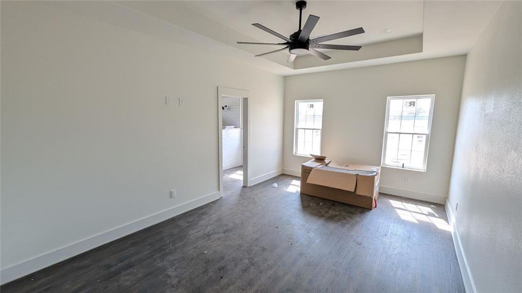 Unfurnished bedroom with a tray ceiling, baseboards, dark wood-type flooring, and ceiling fan