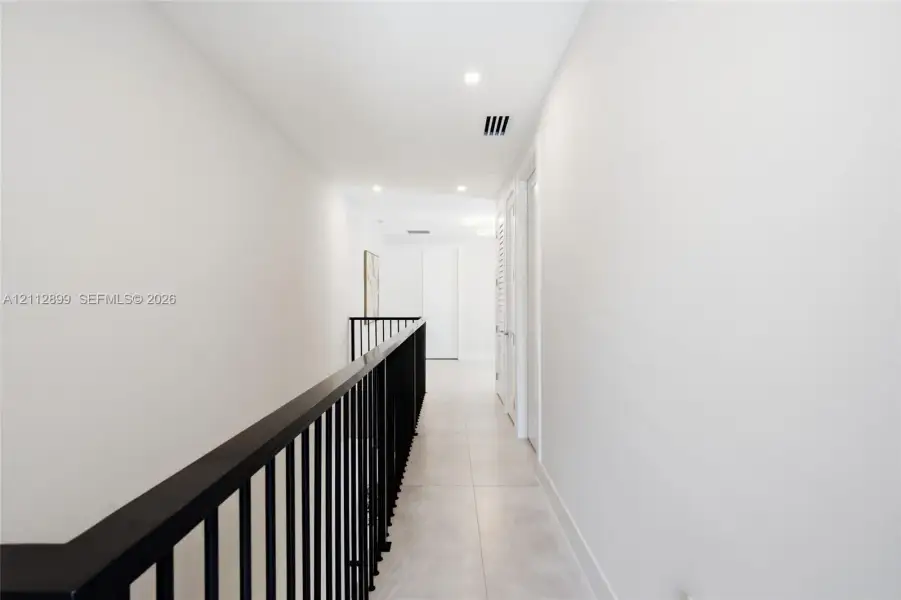 Hallway featuring large-format tile flooring, matte black metal railing, and recessed ceiling lighting