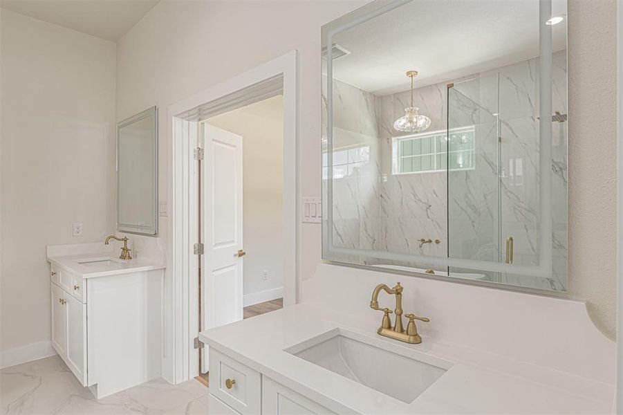 Dual vanity featuring white cabinetry, quartz countertops, and brass-finish fixtures